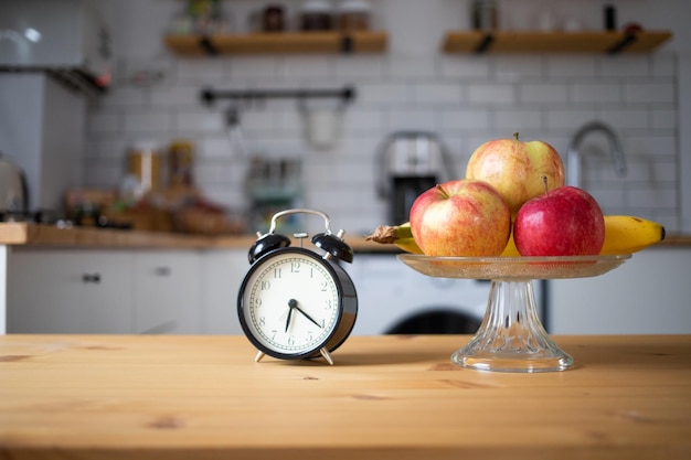 Despertador vintage e frutas frescas na mesa da cozinha em jejum intermitente