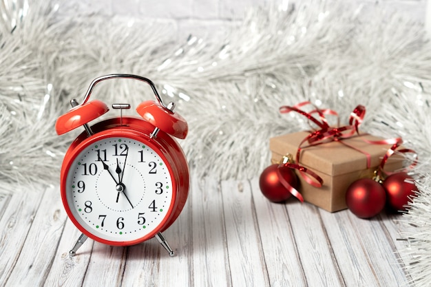 Foto despertador vintage rojo y caja de regalo en una mesa de madera decorada con una guirnalda y bolas rojas de navidad para el año nuevo o navidad. concepto de servicio de correo, mensajería o entrega. copia espacio