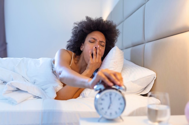 Despertar de una niña dormida que detiene el despertador en la cama por la mañana mujer durmiendo y despierta para apagar el despertador por la mañana