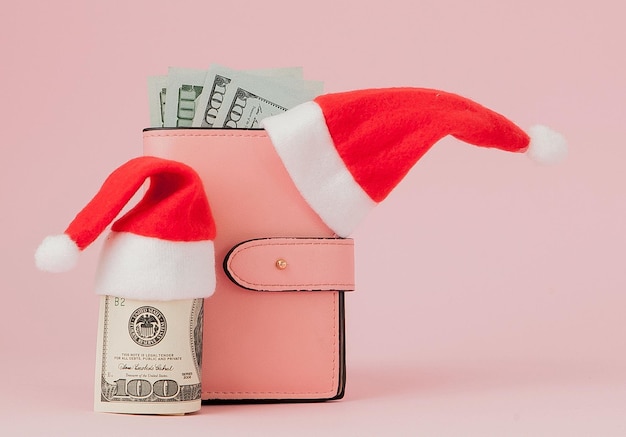 Despesas de Natal Bolsa de couro rosa com chapéu de papai noel árvore de abeto e notas de dólares em fundo rosa Compras de natal Venda de férias