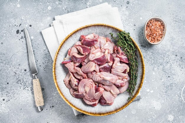 Despojos de estómago de pollo crudo en un plato con hierbas Fondo gris Vista superior