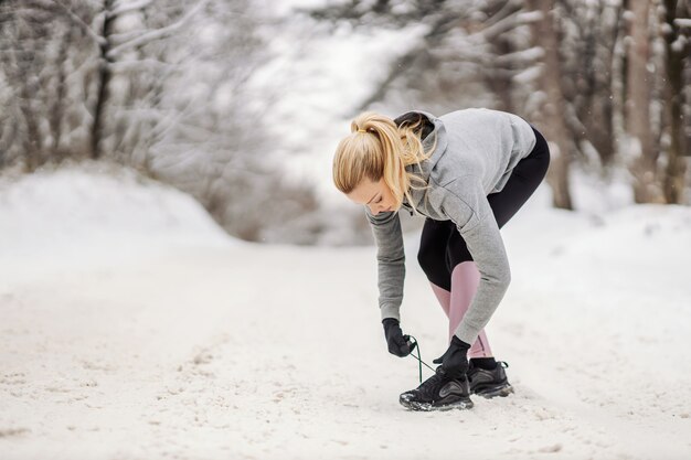 Desportista, amarrar o cadarço em pé no caminho de neve no dia de inverno.