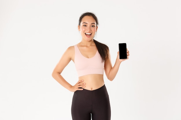 Desportista asiática alegre animada, corredor mostrando sua melhor pontuação em execução no aplicativo do smartphone, demonstra a tela do telefone móvel com o aplicativo de treino.