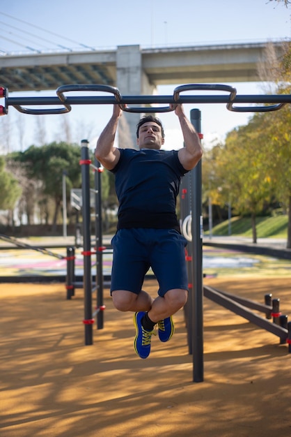 Desportista atraente malhando em dia ensolarado. Roupas esportivas de homem no campo de esportes ao ar livre, puxando as barras. Esporte, saúde, trabalhando o conceito