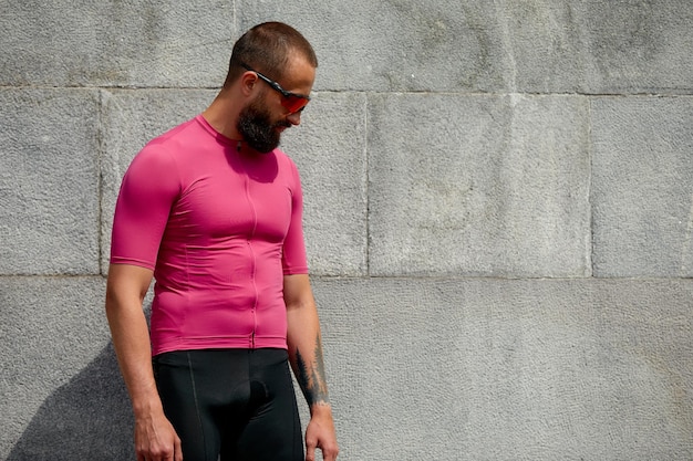 Desportista cansado em roupas esportivas rosa descansando depois de um treino em pé contra o fundo da parede de cimento com área de espaço de cópia para mensagem de texto ou corredor de publicidade fazendo pausa após a corrida