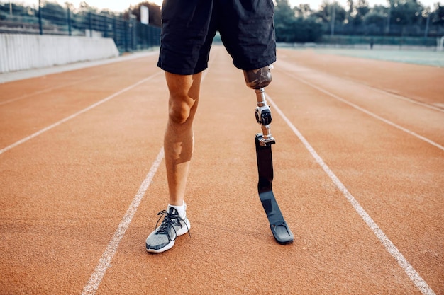 Desportista com perna artificial em pé na pista de corrida no estádio Pernas na pista de corrida