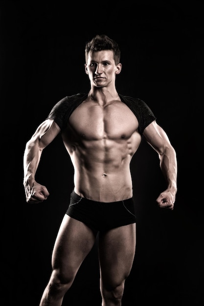 Desportista de homem mostra corpo musculoso em fundo escuro. Fisiculturista com torso nu, tanquinho, ab, bíceps, tríceps, músculos. Esporte, musculação, fitness. Conceito de estilo de vida saudável.