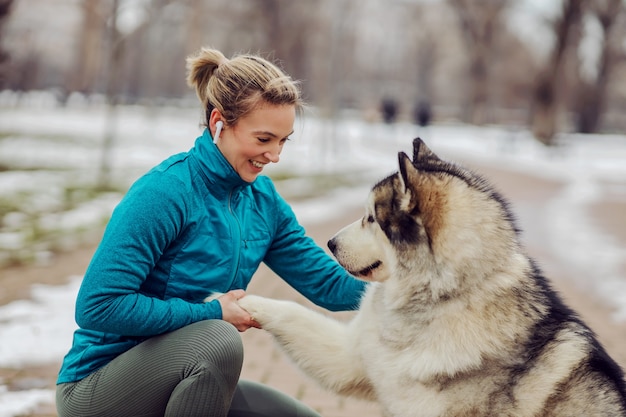 Desportista ensinando seu cachorro a apertar as mãos enquanto se agacha no parque da cidade em clima de neve. Cães, animais de estimação, amor, inverno