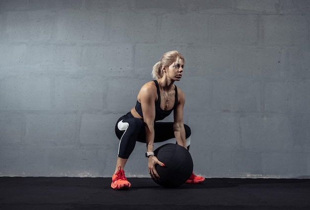 Desportista fazendo exercícios de alongamento com bola medicinal Mulher musculosa exercitando bola de fitness no ginásio