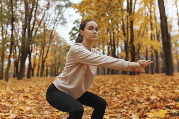 Desportista focada em ajuste fazendo exercício de agachamento enquanto se exercita no parque de outono