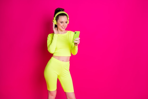 Desportista jovem positiva usar smartphone ouvir lista de reprodução fone de ouvido usar calção amarelo isolado no fundo rosa brilhante