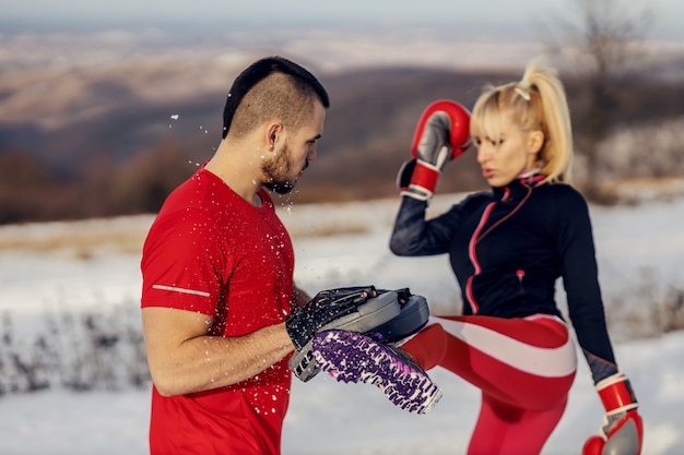 Desportista lutando com luvas de boxe na natureza em um dia de inverno nevado com seu instrutor. Kick-box, fitness de inverno, fitness ao ar livre