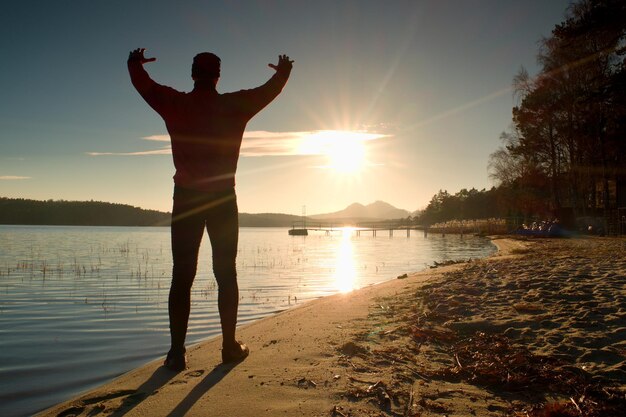 Foto desportista magro na praia com os olhos à sombra e olhando para o sol