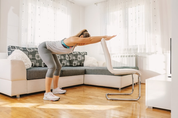 Desportista muscular em forma, fazendo exercícios de fitness para as costas enquanto se inclina na cadeira.