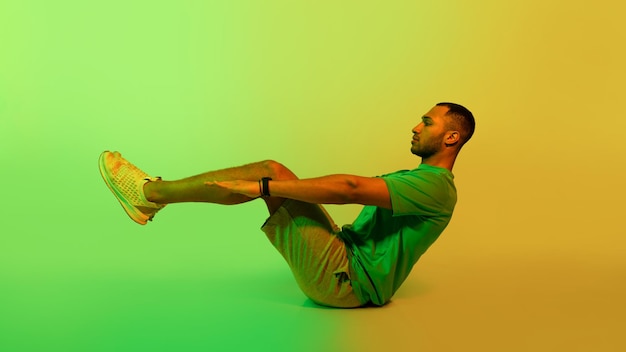 Desportista negro fazendo exercício abdominal vups sentado sobre fundo verde