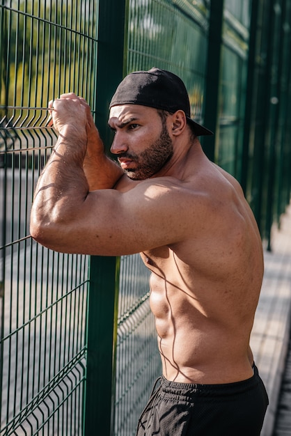 Desportista "sexy" da aptidão que levanta em um campo de esportes em topless. Fitness, musculação, estilo de vida saudável