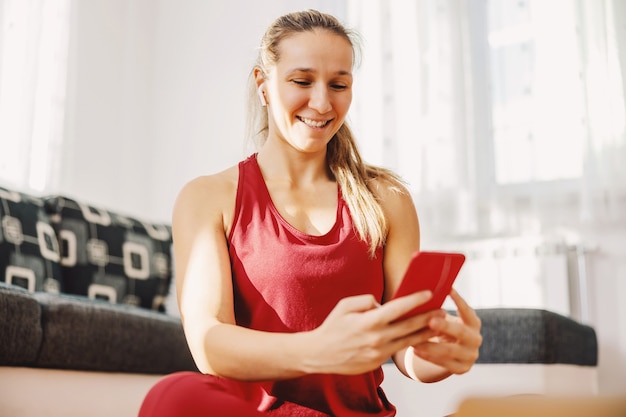 Desportista sorridente, sentada no chão em casa e pendurada nas redes sociais.