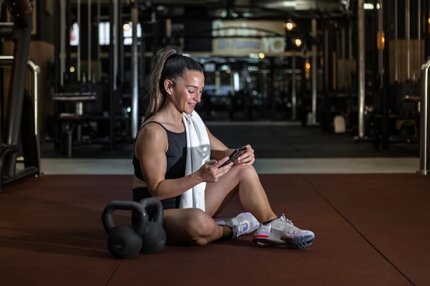 Desportista sorridente usando smartphone enquanto descansava após o treino no ginásio