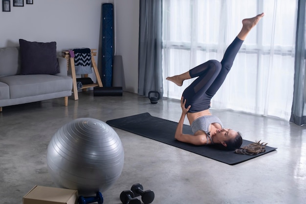 Desportiva jovem mulher asiática fazendo ioga na sala de estar jovem mulher em roupas esportivas se exercitando em casa assistindo treinamento de aula de fitness on-line na sala de estar