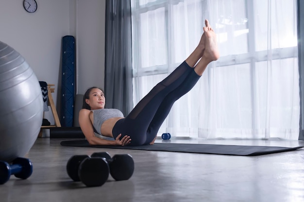 Desportiva jovem mulher asiática fazendo ioga na sala de estar jovem mulher em roupas esportivas se exercitando em casa assistindo treinamento de aula de fitness on-line na sala de estar