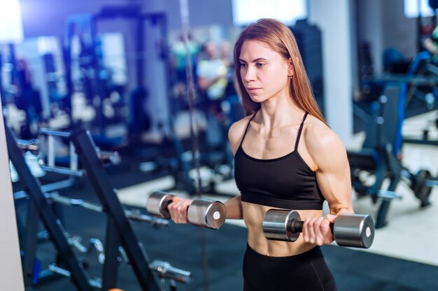 Desportiva mulher fazendo exercícios com halteres, olhando para o futuro no ginásio