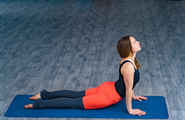 Desportiva mulher praticando ioga, fazendo exercício azul esteira no centro desportivo. Linda fêmea magro no sportswear confortável, deitado em posição de posição com base nas mãos no estúdio de yoga.