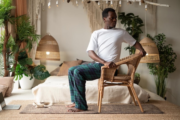 Desportivo jovem africano praticando ioga usando cadeira fazendo pose de cadeira giratória parivrtta utkatasana