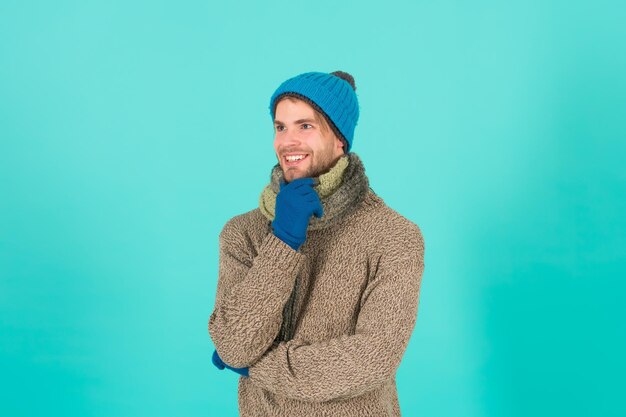 Despreocupado y feliz. Hombre guapo sin afeitar llevar accesorios de invierno sobre fondo azul. Venta de temporada de invierno. Guantes y bufanda de gorro de invierno de punto hipster. Concepto de compras. Expresión emocional.