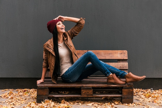 Despreocupado y muy feliz. Hermosa mujer joven sentada en la plataforma de madera