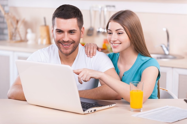 Despreocupado na manhã de domingo. jovem bonito em roupão de banho trabalhando em um laptop em pé na cozinha