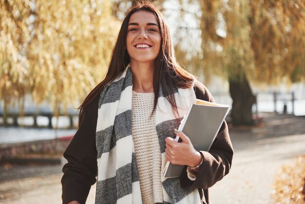 Después de aprobar con éxito el examen. Alegre hermosa chica morena sostiene el bloc de notas mientras descansa después de estudiar