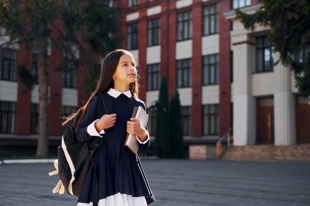 Después de las lecciones, la colegiala está afuera cerca del edificio de la escuela.