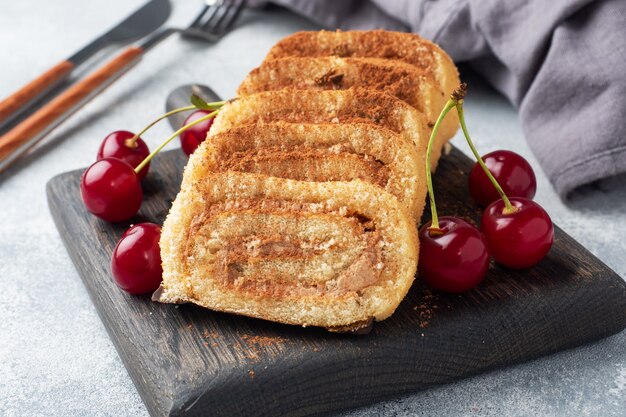 Dessert Biskuitrolle mit Schokoladencreme mit Kirschen auf einem Holzbrett.