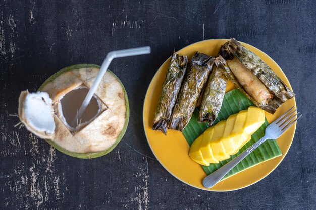 Dessert im thailändischen Stil, gelbe Mango mit klebrigem Bananenreis in Palmblättern. Gelbe Mango und klebriger Reis ist ein beliebtes traditionelles Dessert von Thailand. Nahaufnahme