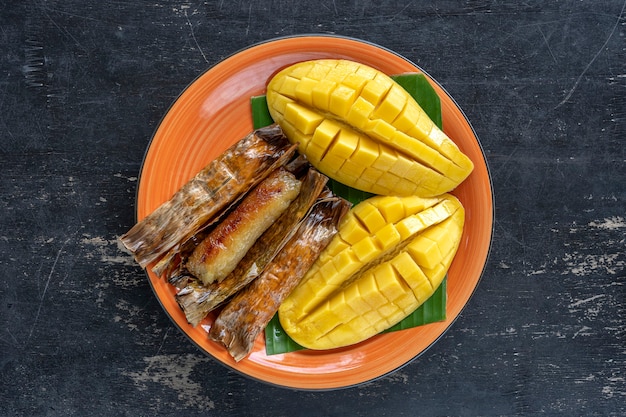 Dessert im thailändischen Stil, gelbe Mango mit klebrigem Bananenreis in Palmblättern. Gelbe Mango und klebriger Reis ist ein beliebtes traditionelles Essen Thailands. Nahaufnahme