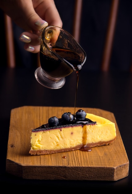 Foto dessert-käsekuchen mit blaubeeren, bestreut mit soße auf dunklem hintergrund