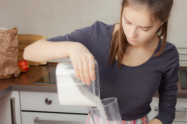 Dessert kochen. Mädchen gießt Kristallzucker in einen Messbecher in der Küche.