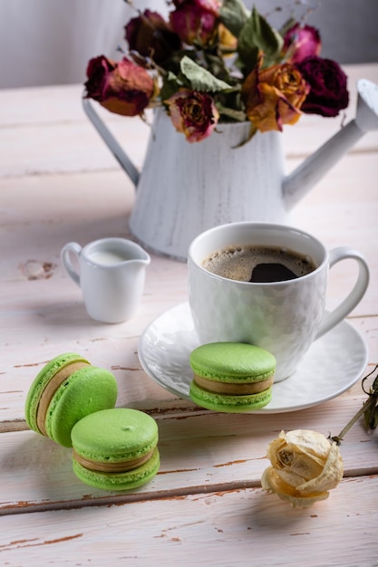 Dessert mit französischen Makronen Drei grüne Makronen und eine weiße Tasse Kaffee auf einem weißen Holztisch