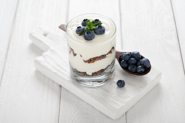 Dessert mit Hüttenkäse, frischen Heidelbeeren und Müsli in einem Glas auf weißem Holzhintergrund