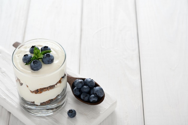 Dessert mit Hüttenkäse, frischen Heidelbeeren und Müsli in einem Glas auf weißem Holzhintergrund