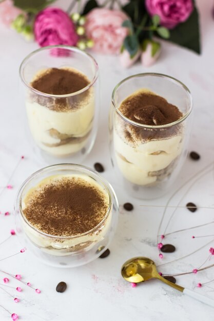 Dessert Tiramisu mit Mascarone und Savojardi auf einer weißen Oberfläche in Gläsern mit doppeltem Boden