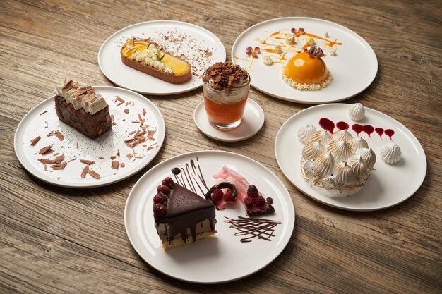Desserttisch mit Cupcake, Mousse, Keksen, Käsekuchen. Stück Kuchen auf einem weißen Teller auf Holztischhintergrund