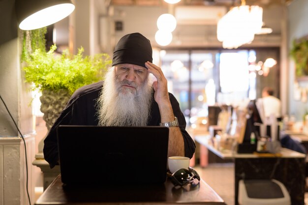 Destacó el hombre hipster barbudo maduro que tiene dolor de cabeza mientras usa la computadora portátil en la cafetería.