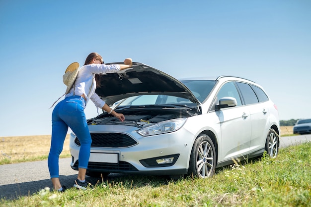 Destacó la mujer joven mirando el motor de su coche. Problemas de viaje por carretera. El coche necesita una reparación.