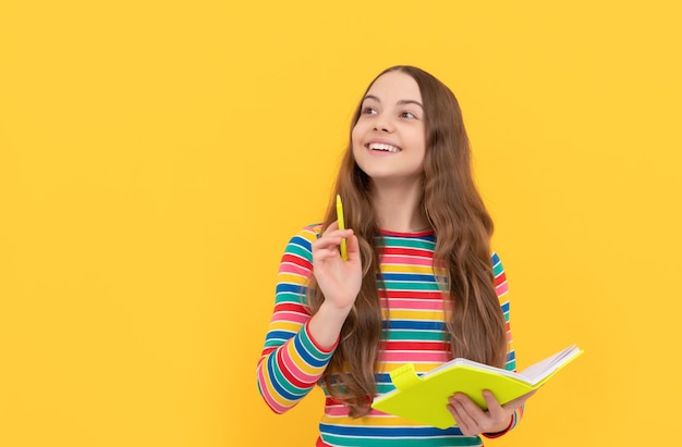 Destello de genio Niña feliz sostener cuaderno apuntando pluma hacia arriba Niño genio fondo amarillo