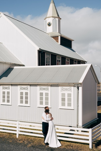 Foto destino islandia boda novios cerca de una iglesia de madera negra el novio abraza a la novia