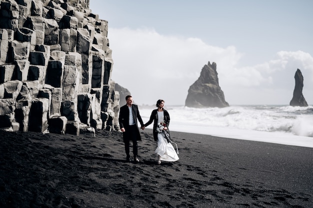 Destino, Islândia, casamento, um casal de noivos caminha pela praia negra de vik