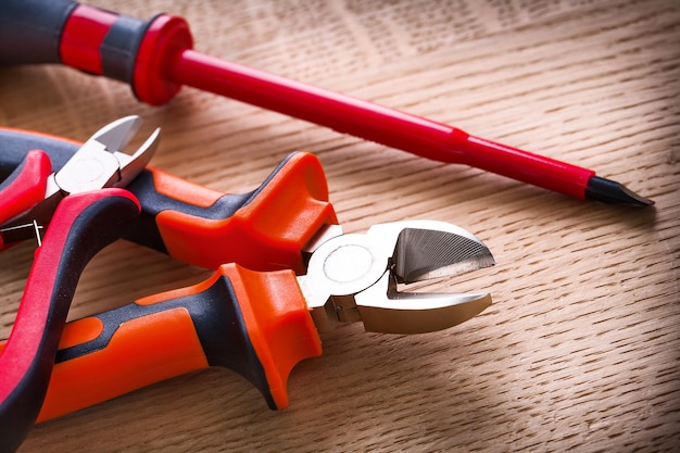 destornillador eléctrico rojo aislado y dos pinzas sobre tabla de madera