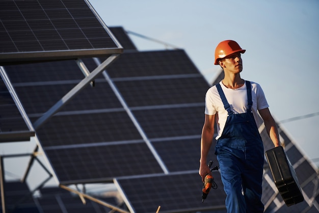 Destornillador inalámbrico en mano. Trabajador de sexo masculino en uniforme azul al aire libre con baterías solares en un día soleado.