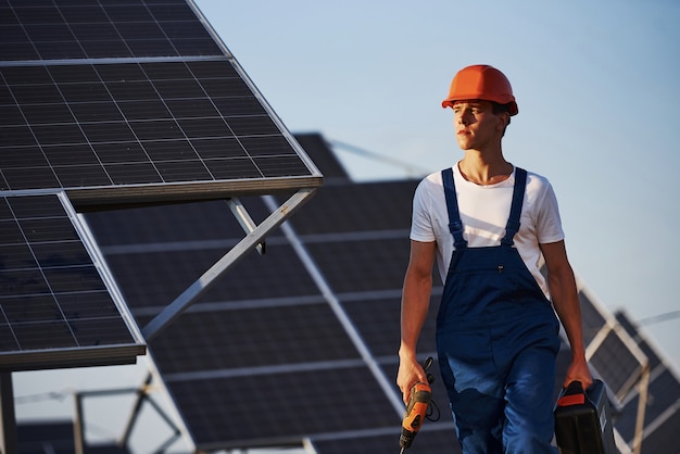 Destornillador inalámbrico en mano. Trabajador de sexo masculino en uniforme azul al aire libre con baterías solares en un día soleado.